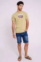 Remera color verde con estampa rectangular de paisaje de flores y montañas.