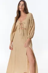 Vestido color beige de lino, con escote en V, mangas largas abullonadas y lazos frontales. Tiene corte a la cintura y falda larga con tajo frontal.