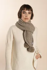 Bufanda tejida a mano en punto arroz color beige, con pompones en los extremos.