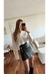 Minifalda negra de cuero sintético con corte irregular y detalle de hebillas decorativas en el lateral.