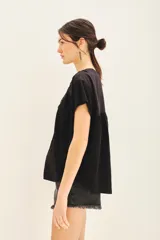 Camisa negra de manga corta con combinación de tejido de punto y plano, detalles de volados y frunces en pechera y espalda, acceso con botones fake nacar y medallita marcaria en espalda.