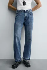 Pantalón de jean celeste de corte flare, con tiro medio, cinco bolsillos, cierre frontal con cremallera y botón, y bajo con acabado irregular.