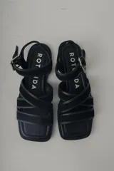 Sandalia plana de cuero color verde militar, con tiras cruzadas en el empeine y una tira ajustable con hebilla metálica dorada en el tobillo.