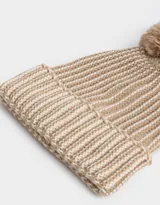 Gorro de lana tejido a crochet en color beige con detalles en blanco y pompón de piel sintética en la parte superior.