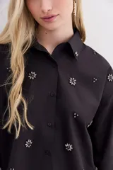 Camisa negra holgada de corte clásico, con cuello camisero, mangas largas con puños y bordados de piedras.