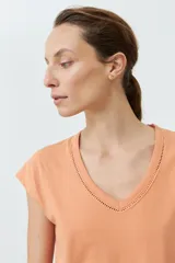 Remera color durazno con cuello en V y detalle de trenza en el escote.
