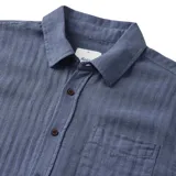 Camisa de manga corta azul con botones marrones y bolsillo en el pecho.