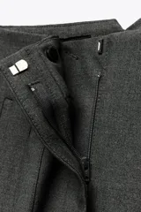Pantalón tobillero color gris claro, de tiro alto, con bolsillos delanteros de vivo y cierre frontal con cremallera, botón interior y gancho metálico.