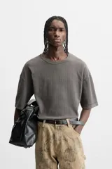 Camiseta color gris verdoso de punto tejido en hilatura de algodón, con cuello redondo, manga corta, efecto lavado y acabados irregulares.