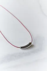 Gargantilla con tiento de hilo encerado color borgoña y dije de acero quirúrgico hipoalergénico plateado en forma de tubo.