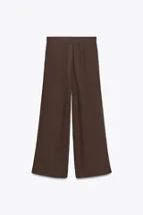 Pantalón marrón de tiro medio, corte ancho y largo cropped. Confeccionado en algodón, con cintura con trabillas y elástico en la espalda, bolsillos laterales y traseros, pinzas en el delantero y cierre frontal con cremallera, botón y ganchos metálicos.