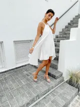Vestido corto color naranja, con escote halter y diseño asimétrico con capas. Espalda con tiras regulables.
