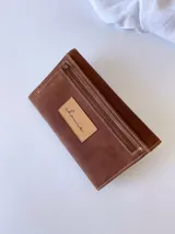 Billetera de cuero marrón con sistema de cierre con broche, monedero externo y detalle de hojas grabadas en la solapa.