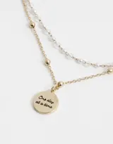 Collar corto dorado de doble cadena, una con cuentas pequeñas y otra con bolitas. Dije redondo esmaltado en blanco con diseño de sol y estrellas.