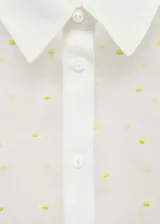 Camisa blanca semitransparente con bordado de flores amarillas, de manga corta, corte recto y cuello camisero.