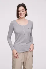 Remera de manga larga entallada en color blanco, confeccionada en algodón. Presenta cuello redondo con una hilera de botones frontales y un pequeño bolsillo en el pecho con detalle de botón.