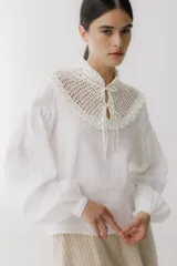 Blusa color ladrillo con cuello alto de crochet y lazos para ajustar. Mangas largas abullonadas con puños elásticos.