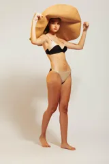 Conjunto de bikini de dos piezas con corpiño triangular negro con tirantes finos y detalle de contorno en color beige. La bombacha es de corte clásico en color beige.