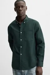Camisa azul marino de corte regular fit, confeccionada en tejido de algodón Oxford. Tiene cuello abotonado, manga larga con puños abotonados, bolsillo de parche en el pecho y cierre frontal con botones.