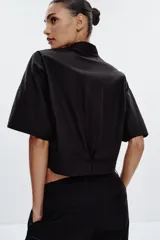 Camisa negra de popelín con cuello solapa y manga ancha por debajo del codo. Detalle de pinzas en la espalda y cierre frontal con botones ocultos por solapa.
