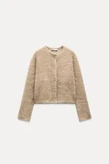 Chaqueta color beige de tejido de punto con efecto pelo, cuello redondo, manga larga y cierre frontal con botones tipo perla.