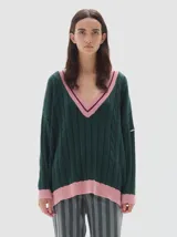 Buzo tejido oversized color verde oscuro con cuello en V, ribeteado en rosa claro y bordó. Tiene mangas largas y un diseño de trenzas en el tejido. El bajo y los puños también están ribeteados en rosa claro.