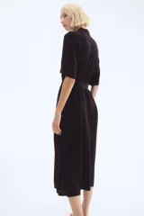 Vestido midi negro con cuello camisero, mangas cortas tipo raglán y botonadura frontal. Presenta elástico en la cintura y cinturón extraíble para atar.