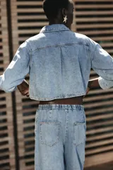 Camisa corta de denim celeste, con cuello solapa, manga larga, bolsillo delantero de plastrón y cierre frontal con botones metálicos.