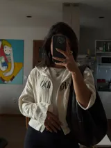 Campera color crudo de tejido de punto con cierre frontal y estampado con la palabra "Ardido" en negro.