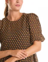 Blusa peplum marca Nanette, color negro con estampado de lunares dorados. Tiene escote a la base, mangas cortas con frunce y abertura con botón en la espalda. Incluye una musculosa interna a tono.