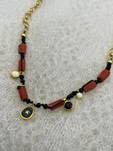 Collar corto con cadena dorada y dijes colgantes de coral, perlas y dijes dorados con detalles en negro.