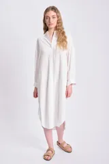 Vestido camisero largo color blanco, con cuello mao, abotonadura frontal y mangas largas abullonadas con puños camiseros.