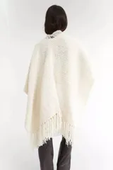 Ruana color crema tejida a mano con cuello con detalle de crochet y flecos en el ruedo.