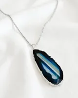 Collar con cadena de acero plateado y dije de piedra ágata con borde plateado y vetas en tonos azul, celeste y blanco.