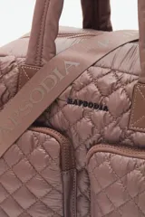 Bolso marrón con diseño matelassé, doble asa corta, correa larga desmontable y dos bolsillos frontales. Incluye llavero de corazón y dijes desmontables.