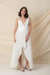 Vestido blanco de crepe con escote profundo y falda irregular con flecos brillantes. Se puede usar con pantalones por debajo.