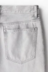 Pantalón jean gris claro, de corte holgado con pierna ancha y tiro bajo. Diseño clásico de cinco bolsillos con cierre frontal con cremallera y botón.