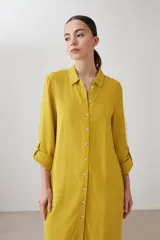 Vestido camisero midi color mostaza, de lino, con cuello camisero, mangas 3/4 con trabillas y cierre frontal con botones.