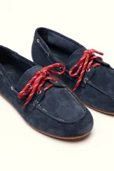 Mocasín tipo boat shoe con estampado de vaca en tonos marrón y blanco, confeccionado en cuero. Cuenta con cordones de cuero marrón oscuro y suela de goma.