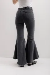 Pantalón de jean negro elastizado con corte ajustado y volados en la parte baja de la pierna. El ruedo es más largo en la parte trasera y tiene terminación descosida.