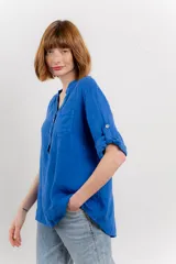 Camisa azul de lino con escote en V abotonado, bolsillo frontal y mangas 3/4 con trabilla.