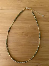 Collar corto con cuentas facetadas color verde oscuro y tubos dorados. Cierre de mosquetón con cadena de alargue y dije de cristal.