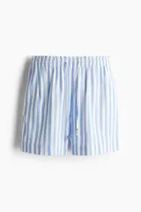 Short holgado de tiro alto, confeccionado en tejido liviano de lino y viscosa a rayas verticales celestes y blancas. Presenta cintura elástica fruncida con ribete de volado, cordón de ajuste con cuentas metálicas y bolsillos laterales.