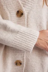 Cardigan de punto color crema, con escote en V, cierre frontal con botones marrones y corte holgado.