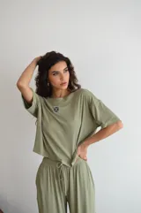 Remera de manga corta color crema, con textura acanalada y cuello redondo. Presenta un pequeño parche bordado con un diseño floral o geométrico en el pecho.