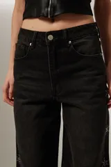 Pantalón jean negro de corte ancho y tiro alto, con bolsillos y apliques de strass en forma de estrella en los laterales.