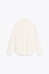 Camisa color crema de corte recto, confeccionada en algodón. Tiene cuello solapa, manga larga con puños abotonados, bolsillo de parche en el pecho y cierre frontal con botones.