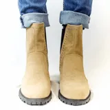 Bota Chelsea blanca de cuero sintético con elástico lateral negro adornado con tachas plateadas. Tiene suela track negra y taco bajo.