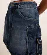 Minifalda de jean celeste con efecto marmolado, trabillas en la cintura, cierre frontal con botón y bolsillos cargo laterales con lazos y hebillas.