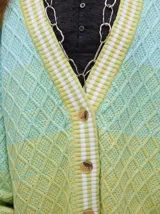 Cardigan tejido de punto con patrón de rombos en degradé de grises y blanco. Tiene corte oversize, mangas largas y cierre frontal con botones.